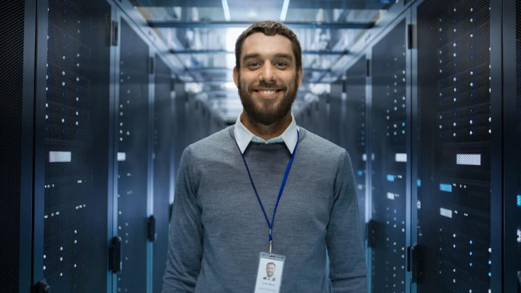 Portrait of IT Engineer Standing in the Middle of a Large Data Center Server Room.