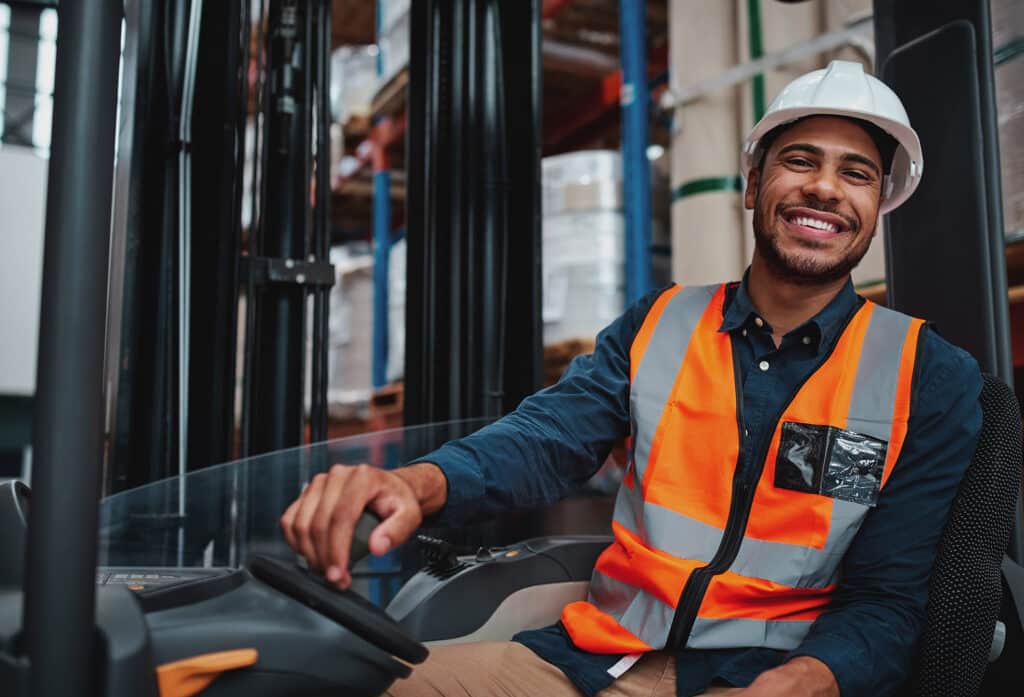 Happy forklift driver sitting in vehicle in warehouse
